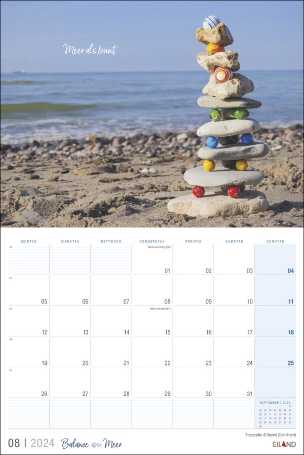 Ein Balance am Meer-Kalender 2024, prekär arrangiert mit einem Steinhaufen am ruhigen Strand.