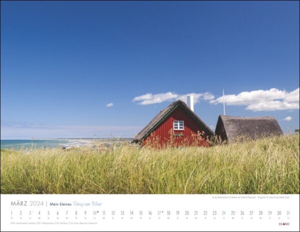 Ein Kalender mit „Mein kleines Haus am Meer 2024“ auf einem grasbewachsenen Hügel.