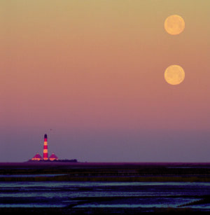 Drei Monde über einem Leuchtturm an der Küste - Naturparadies Wattenmeer.