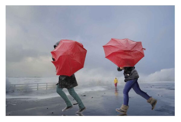Zwei Menschen laufen mit roten Regenschirmen durch den Schietwetter-Regen.