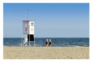 Zwei Menschen gehen am Strand in der Nähe eines Rettungsschwimmerturms im Küstenland spazieren - Ein morgendliches Bad hält jung...