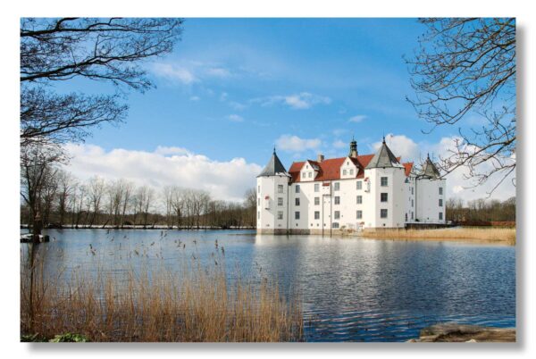 Ein weißes Schloss, Schloss Glücksburg, liegt neben einem Gewässer.