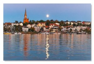 Der Mond geht über der Stadt Schleswig-Holstein - Flensburg mit Booten auf dem Wasser auf.