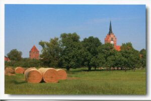 Heuballen auf einem Feld mit einer Kirche im Hintergrund auf der Insel Usedom - Meine Insel - Stadt Usedom mit Stadttor und St. Marienkirche.