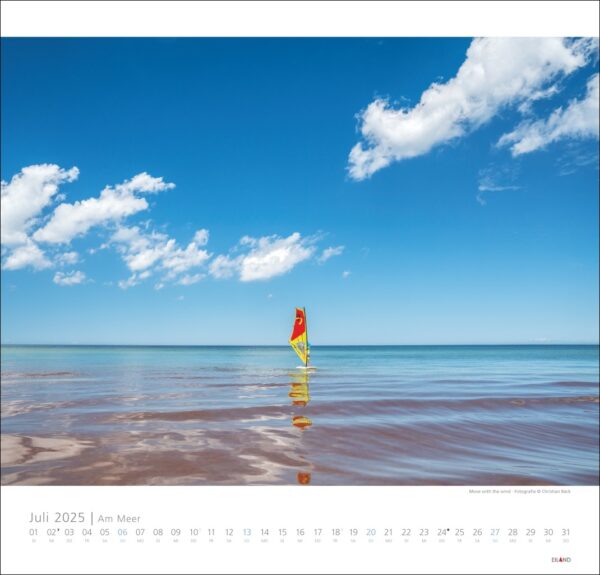 Eine Kalenderseite für „Am Meer 2025“ mit einer heiteren Strandszene: klarer blauer Himmel, ruhiges Meer und ein einsames buntes Windsurfbrett im nassen Sand, das sich im seichten Wasser unter „Am Meer 2025“ spiegelt.