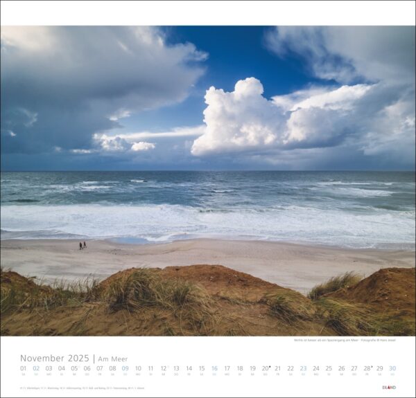 Eine Kalenderseite für Am Meer 2025 mit einer Strandszene „Am Meer“ mit einem riesigen bewölkten Himmel und rauen Meereswellen. Zwei kleine Figuren in der Ferne gehen in der Nähe des Wasserrands, von hinten betrachtet