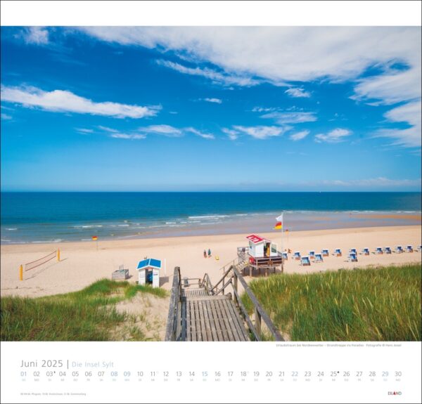 Ein Kalenderbild für Die Insel Sylt 2025 mit einem malerischen Strandblick auf der Insel Sylt. Ein Holzsteg führt zu einem Sandstrand mit wenigen Strandbesuchern, strahlend blauem Himmel und einem