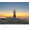 Ein heiteres Kalenderbild für Dezember 2025 mit einem rot-weißen Leuchtturm, Teil der Serie „Faszination Leuchttürme – An den Grenzen der Landschaft 2025“, auf einem grasbewachsenen Hügel bei Sonnenaufgang.