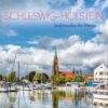 Eine malerische Aussicht auf [Produktname] mit einem Hafen mit Segelbooten, einem markanten Kirchturm mit grüner Spitze, weißen Häusern und einem bewölkten blauen Himmel. Bildunterschrift: