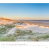 Eine malerische Seite für Schleswig-Holstein 2025 für Januar, mit einem ruhigen Strand mit weichen, grasbewachsenen Dünen unter einem hellblauen Himmel, der in einen pastellfarbenen Sonnenuntergang über einem ruhigen Meer übergeht.