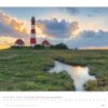 Eine landschaftlich reizvolle Kalenderseite für Schleswig-Holstein 2025 zeigt einen großen rot-weiß gestreiften Leuchtturm in Schleswig-Holstein, Deutschland. Ein kleiner Bach schlängelt sich durch eine üppige grüne Wiese darunter.