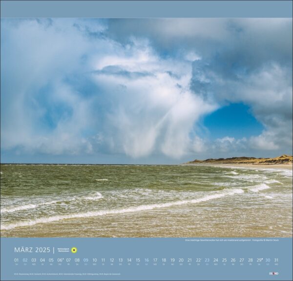 Eine Kalenderseite für den Nationalpark Wattenmeer 2025 mit dem Nationalpark Wattenmeer, die eine dramatische Küstenlandschaft unter einem bewölkten, blauen Himmel zeigt, mit Sonnenstrahlen, die durch die Wolken dringen und die rauen Meereswellen beleuchten.
