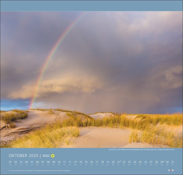 Ein malerischer Nationalpark Wattenmeer-Kalender 2025 für Oktober, der einen leuchtenden Regenbogen zeigt, der sich über einen stürmischen Himmel über dem ruhigen Nationalpark Wattenmeer wölbt, mit sanften Sanddünen, die mit goldenem Gras bedeckt sind.