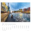 Ein Hansestadt Hamburg - PostkartenKalender 2025 mit einem lebendigen Foto des Hansestadt Hamburger Stadtteils HafenCity. Das Bild zeigt moderne Gebäude entlang eines Kanals mit Eisbrocken unter einem dynamischen Himmel.