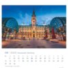 PostkartenKalender Kalenderseite mit April 2025 für die Hansestadt Hamburg. Zeigt ein lebendiges Foto des Hamburger Rathauses mit einem beleuchteten Glockenturm in der Abenddämmerung, eingerahmt von einer gewölbten Glasstruktur. Daten und