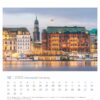 Eine Seite des Hansestadt Hamburg - PostkartenKalenders 2025 für Dezember mit einer Szene des Hamburger Rathauses in der Dämmerung, einem historischen Gebäude mit einem zentralen Uhrenturm, der entlang einer reflektierenden Wasserfläche wunderschön beleuchtet ist.