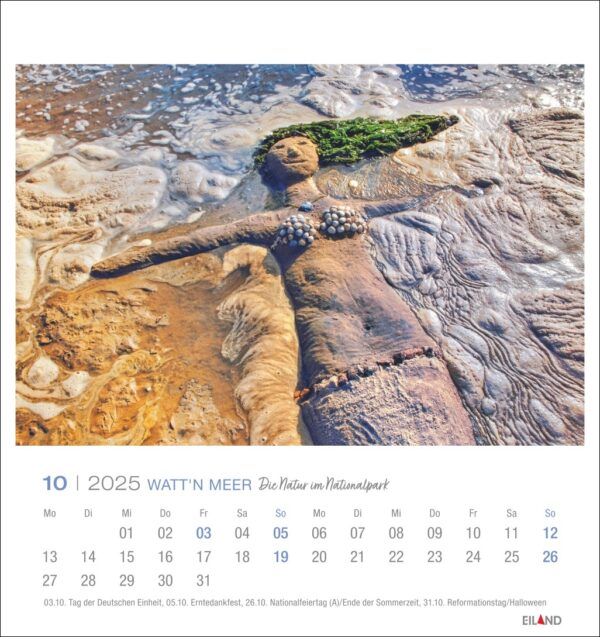 Eine kreative Sandskulptur einer Meerjungfrau mit grünem Seetanghaar und einer Muschelkette liegt an einem Strand, abgebildet auf einer Kalenderseite „Watt’n Meer – PostkartenKalender 2025“ vom Oktober 2025 mit deutschem Text.
