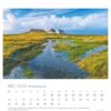 Eine Nordseeküste - PostkartenKalender-Seite für März 2025 mit einer ruhigen Küste, mit einem von üppigem Grün umgebenen Wasserkanal, in der Ferne traditionellen Häusern unter einem blauen Himmel mit flauschigen Wolken.