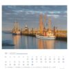 Eine Nordseeküste - PostkartenKalender 2025 Seite für November mit einer ruhigen Hafenszene bei Sonnenuntergang. Zwei Fischerboote liegen an einem ruhigen Wasserweg vor Anker, unter einem sanft leuchtenden Himmel, mit einem Leuchtturm in der Ferne