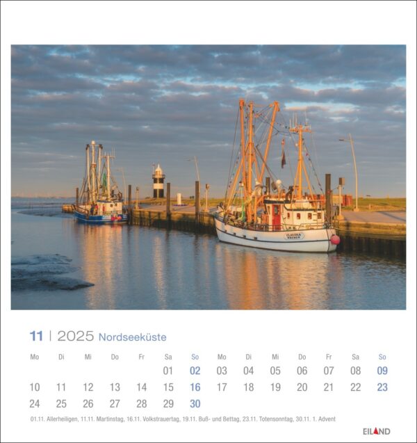 Eine Nordseeküste - PostkartenKalender 2025 Seite für November mit einer ruhigen Hafenszene bei Sonnenuntergang. Zwei Fischerboote liegen an einem ruhigen Wasserweg vor Anker, unter einem sanft leuchtenden Himmel, mit einem Leuchtturm in der Ferne