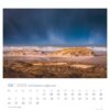 Eine Seite des PostkartenKalenders 2025 „Ostfriesland einfach schön“ für Februar mit einem dramatischen Foto einer Strandlandschaft in Ostfriesland, das goldenes Sonnenlicht zeigt, das Sanddünen vor einem stürmischen Himmel beleuchtet.