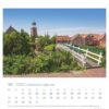 Der Ostfriesland einfach schön - PostkartenKalender 2025 für Oktober zeigt eine malerische Aussicht auf Ostfriesland mit rot gedeckten Häusern und einer Kirche mit grünem Turm. Im Vordergrund ein