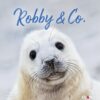 Eine Nahaufnahme eines weißen Robbenjungen mit einer Sandschicht auf der Nase, der direkt in die Kamera blickt. Das Bild zeigt oben den Text „Robby & Co.“ und Robby & Co. - PostkartenKalender 2025.