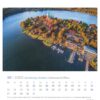 Luftaufnahme einer üppigen, bewaldeten Insel in Schleswig-Holstein - PostkartenKalender 2025 mit einem großen, historischen Gebäude mit rotem Dach und mehreren Nebengebäuden, umgeben von Wasser mit einem Dock und