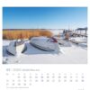Eine Rügen - PostkartenKalender 2025 Seite für Januar mit einer verschneiten Landschaft mit umgekippten Booten neben trockenem Schilf an einem zugefrorenen See unter einem strahlend blauen Himmel. Tage und Daten sind unter dem Kalender aufgeführt.