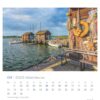 Eine Seite des Rügen - PostkartenKalenders 2025 für April mit einer ruhigen Hafenszene auf der Insel Rügen, Deutschland. Kleine Boote liegen an einem Holzsteg festgemacht, mit einem malerischen Gebäude geschmückt mit