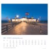 Eine Usedom - PostkartenKalender 2025 Seite für Januar mit der Usedomer Seebrücke in der Abenddämmerung. Ein hell erleuchtetes Gebäude am Ende der Seebrücke wird von Fahnenmasten mit verschiedenen Flaggen flankiert.