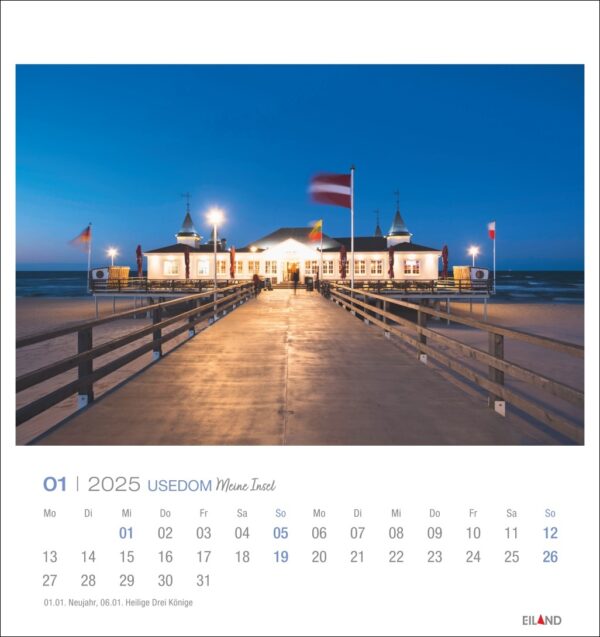 Eine Usedom - PostkartenKalender 2025 Seite für Januar mit der Usedomer Seebrücke in der Abenddämmerung. Ein hell erleuchtetes Gebäude am Ende der Seebrücke wird von Fahnenmasten mit verschiedenen Flaggen flankiert.