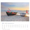 Auf einer Seite des Usedom - PostkartenKalenders 2025 für September sind zwei kleine Boote an einem Sandstrand bei Sonnenuntergang zu sehen. Die mit bunten Flaggen geschmückten Boote liegen teilweise am Ufer, im Hintergrund ist das Meer zu sehen.