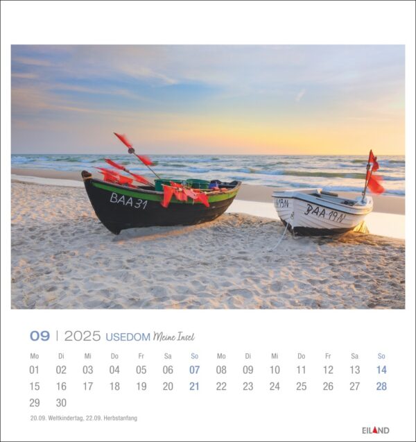 Auf einer Seite des Usedom - PostkartenKalenders 2025 für September sind zwei kleine Boote an einem Sandstrand bei Sonnenuntergang zu sehen. Die mit bunten Flaggen geschmückten Boote liegen teilweise am Ufer, im Hintergrund ist das Meer zu sehen.