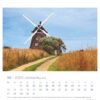Ein Usedom - PostkartenKalender 2025 für Oktober mit einer großen Windmühle umgeben von üppigem Grün und einem klaren blauen Himmel. Die Daten sind unten in Zeilen angeordnet, deutsche Feiertage sind markiert.