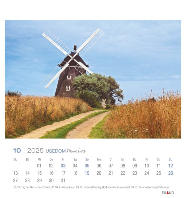Ein Usedom - PostkartenKalender 2025 für Oktober mit einer großen Windmühle umgeben von üppigem Grün und einem klaren blauen Himmel. Die Daten sind unten in Zeilen angeordnet, deutsche Feiertage sind markiert.