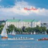 Ein Werbebild für Hamburg mit Segelbooten und Ruderteams auf einem See, mit dem eleganten Hotel Atlantic im Hintergrund unter blauem Himmel. Der Text „Hamburg meine Perle 2025“ überlagert die