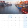 Eine Kalenderseite für Ostfriesland 2025 mit einem malerischen Hafen in Ostfriesland, Deutschland, mit bunten Booten, die bei Sonnenuntergang unter einem klaren Himmel am Wasser vor Anker liegen.