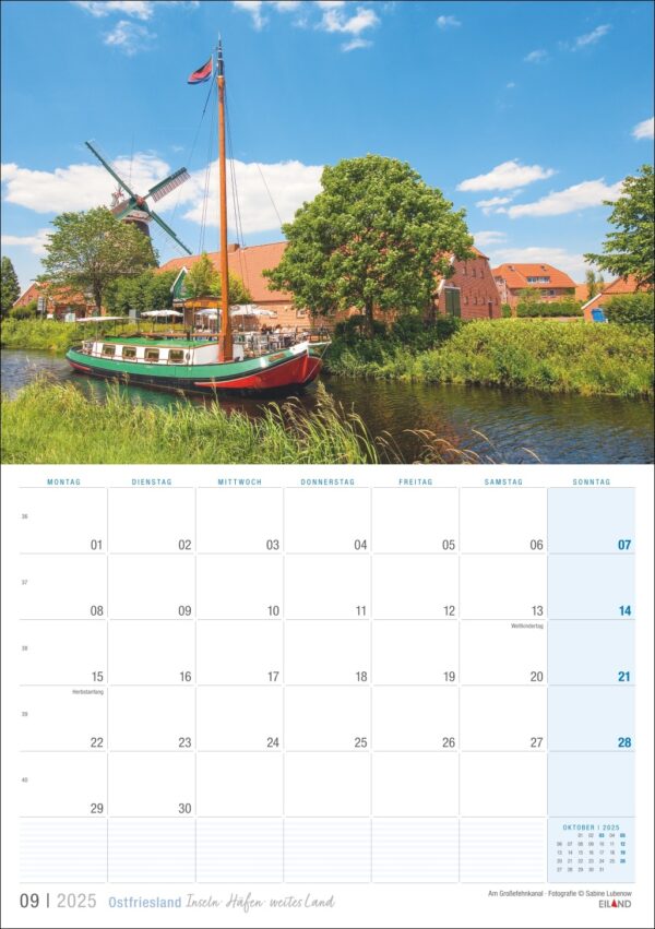 Ostfriesland 2025: Eine landschaftlich reizvolle Kalenderseite für Ostfriesland 2025 zeigt einen ruhigen Fluss mit einem am Ufer vertäuten alten Segelboot. Im Hintergrund steht eine traditionelle Windmühle unter einem klaren blauen Himmel