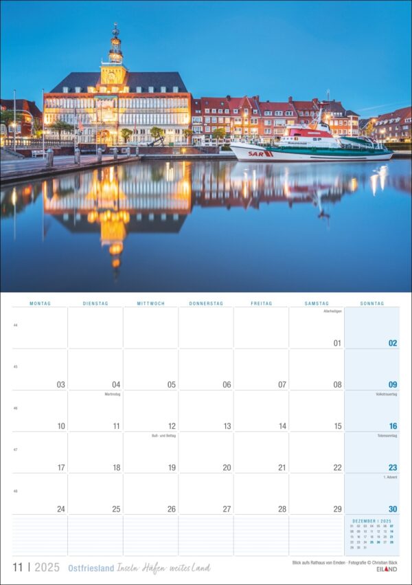 Eine Ostfriesland 2025-Seite für November, die eine Dämmerungsansicht von Ostfriesland mit historischen Gebäuden zeigt, die sich in einem ruhigen Fluss spiegeln. Die Tage sind ordentlich in Reihen angeordnet, mit Wochenenden in Rot. Die Oberseite