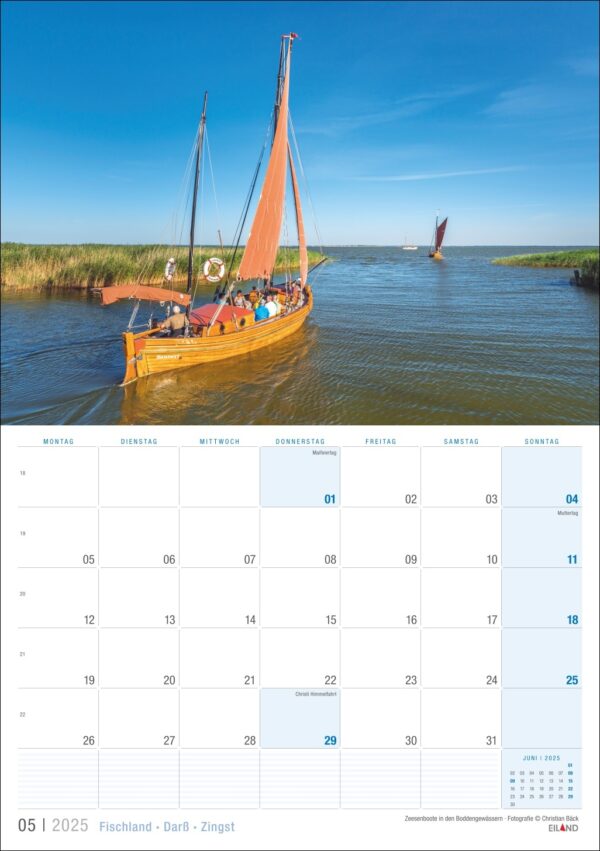 Eine Kalenderseite mit einem ruhigen Bild von zwei Segelbooten mit leuchtend orangefarbenen Segeln, die auf den Gewässern von Fischland · Darß · Zingst gleiten, umgeben von üppigem grünem Schilf unter einem klaren Himmel.