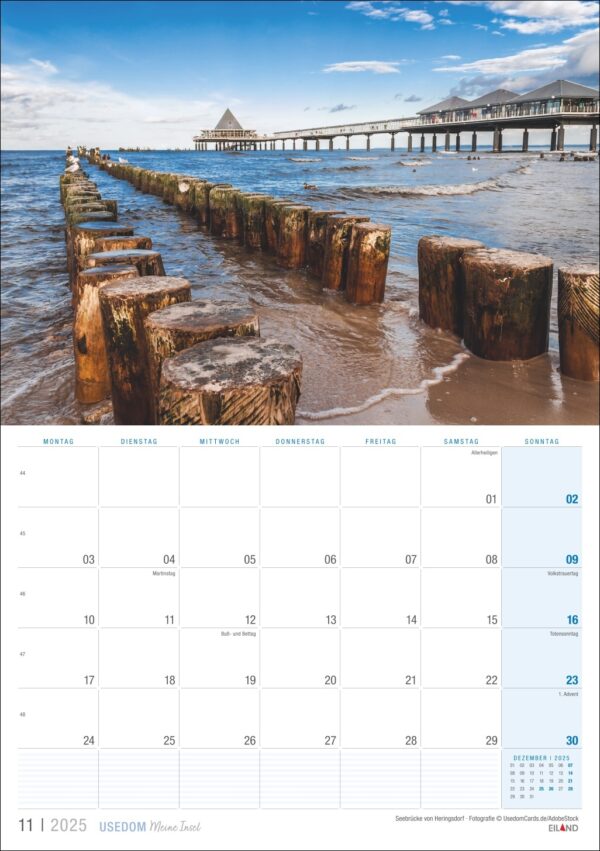 Eine Kalenderseite vom November 2025 mit einem ruhigen Landschaftsfoto von alten Holzpfählen, die über einem ruhigen Meer unter blauem Himmel zu einem entfernten Pier führen, mit der Aufschrift „Usedom … meine Insel 2025“.