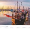Ein Küstenland – Meer erleben-Kalender 2025 mit einer ruhigen Sonnenaufgangsszene an einem Yachthafen in Küstenland, der im Vordergrund ein altes Holzboot und im Hintergrund Yachten zeigt, die sich im stillen Wasser spiegeln.