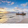 Ein Küstenland - Meer erleben-Kalender 2025 mit einem ruhigen Strand und einem kleinen Boot, das bei Sonnenuntergang unter einem leicht bewölkten Himmel in Ufernähe vor Anker liegt. Die Tage des Monats.