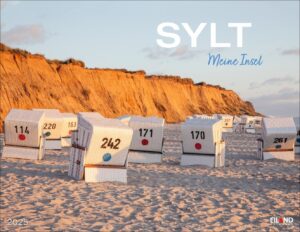 Strandszene auf Sylt - Meine Insel 2025 Insel mit einer Reihe weißer Strandkörbe, einige mit farbigen Punkten, aufgereiht am Sandstrand vor dem Hintergrund einer hohen, sonnenbeschienenen Sandklippe