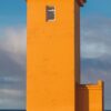 Ein LongEiland - Kalender 2025 für November mit einem leuchtend orangefarbenen Leuchtturm an einer felsigen Küste unter einem blauen Himmel mit vereinzelten Wolken. Die Daten sind auf der rechten Seite und eine Karte mit Islands Lage ist ebenfalls enthalten.