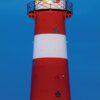 Werbeplakat für „LilleEiland – Kalender 2025“ mit einem lebendigen Bild eines großen rot-weißen Leuchtturms mit Blick auf das Meer vor einem strahlend blauen Himmel