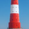 Werbeplakat für LilleEiland - Kalender 2025 mit einem rot-weiß gestreiften Leuchtturm mit herzförmigen Fenstern auf einer Insel, der sich im Wasser darunter spiegelt. Im Hintergrund befindet sich ein Kalender mit markierten Daten und