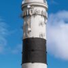 Ein hoher, historischer weißer Leuchtturm mit einem schwarzen Laternenraum und einem Balkon steht unter einem klaren Himmel. Ein LilleEiland - Kalender 2025 für Mai und eine Karte von Deutschland mit der Insel Sylt sind