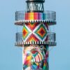 Ein Leuchtturm in einer bunten Hülle mit geometrischem Muster vor einem klaren blauen Himmel, mit einem LilleEiland - Kalender 2025 auf der linken Seite, der den 7. markiert. Der Text enthält